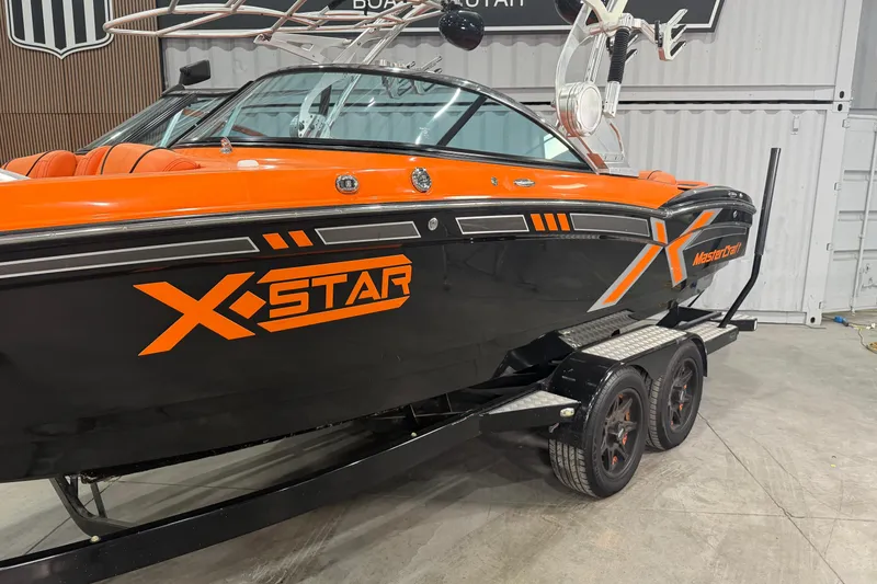 Slide: The Image of 2013 MasterCraft XStar boat with orange and black design on a trailer in a showroom. - 3