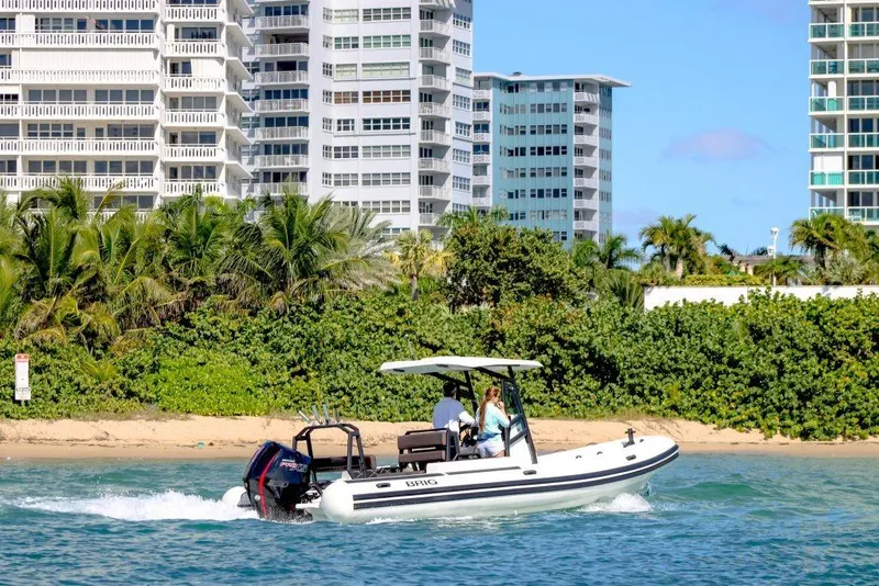 Slide: The Image of 2027 Brig Navigator 24 boat cruising near beachfront buildings and lush greenery. - 1