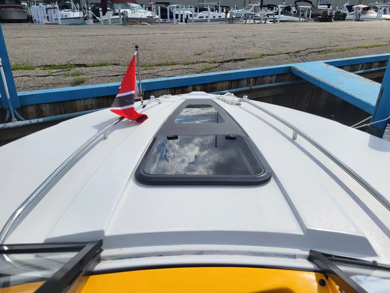 Slide: The Image of A 2014 Glastron GT 229 boat docked in a marina. It features a skylight and a flag. - 3