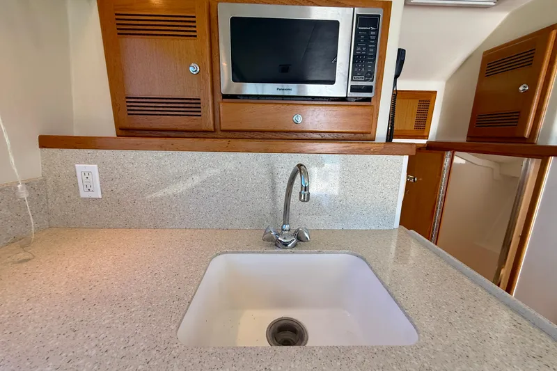 Slide: The Image of 2004 Cabo 35 Flybridge kitchen with sink, microwave, and wooden cabinetry. - 22