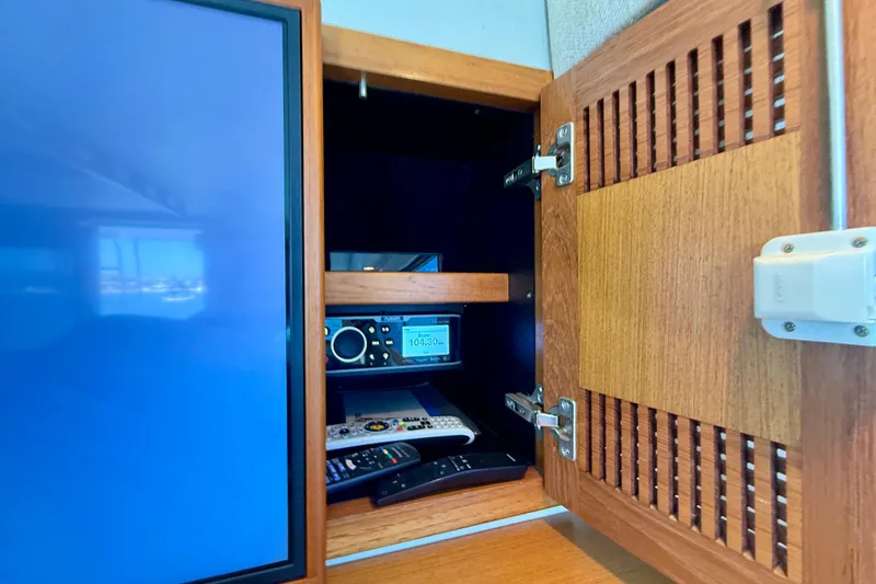 Slide: The Image of Open wooden cabinet on 2004 Cabo 35 Flybridge, revealing electronic equipment and remote controls. - 34