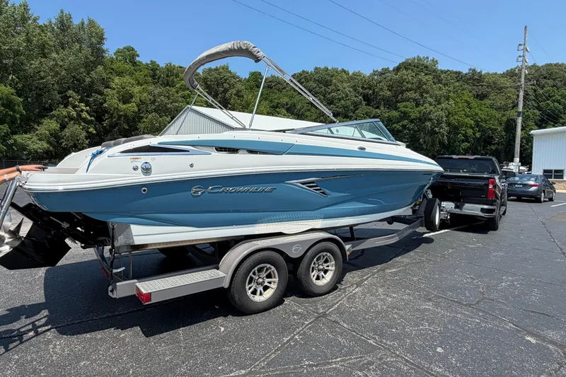 Slide: The Image of 2023 Crownline 240 SS boat on trailer, parked outdoors near trees and buildings. - 3