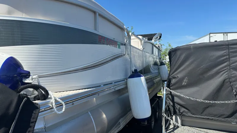 Slide: The Image of A 2008 Manitou Legacy pontoon boat with blue fenders, parked next to a trailer. - 23