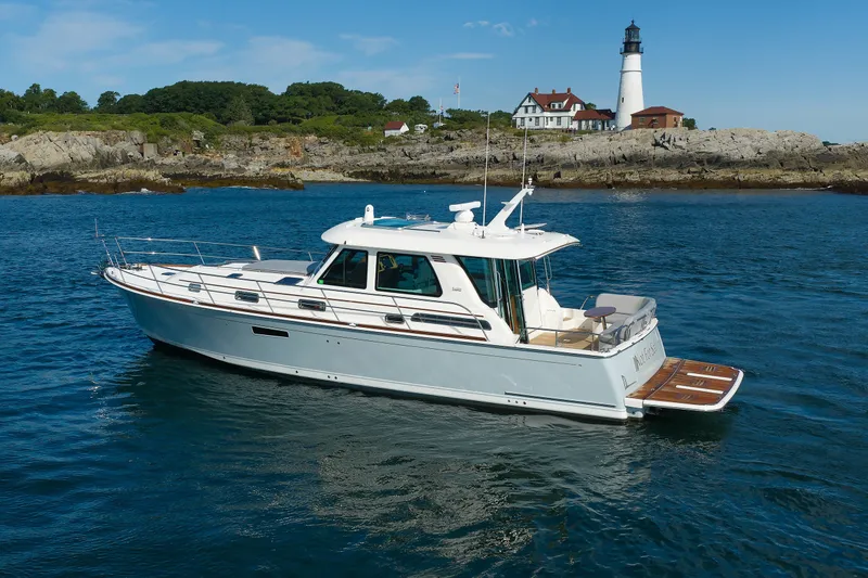 Slide: The Image of 2024 Sabre 48 Salon Express yacht cruising near a scenic lighthouse and rocky shoreline. - 2
