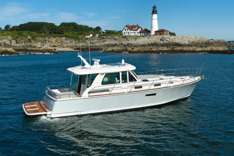 The Image of 2024 Sabre 48 Salon Express yacht cruising near a scenic lighthouse and rocky shoreline. - 0