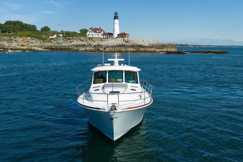 Slide: The Image of 2024 Sabre 48 Salon Express yacht cruising near a scenic lighthouse and rocky coastline. - 4