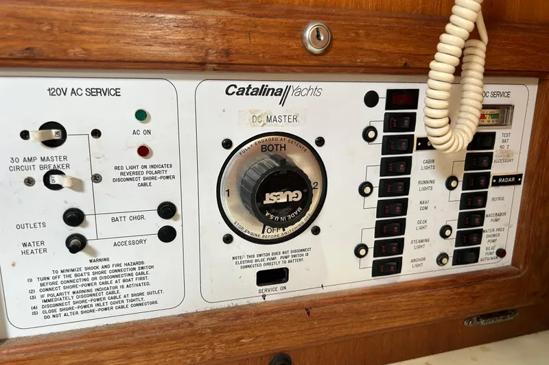 Slide: The Image of Electrical control panel of a 1998 Catalina 36 MkII yacht, featuring AC and DC service switches. - 65
