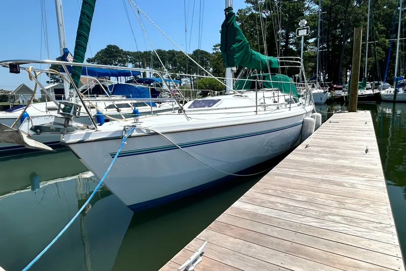 Slide: The Image of 1998 Catalina 36 MkII sailboat docked at a marina, surrounded by trees and other boats. - 1