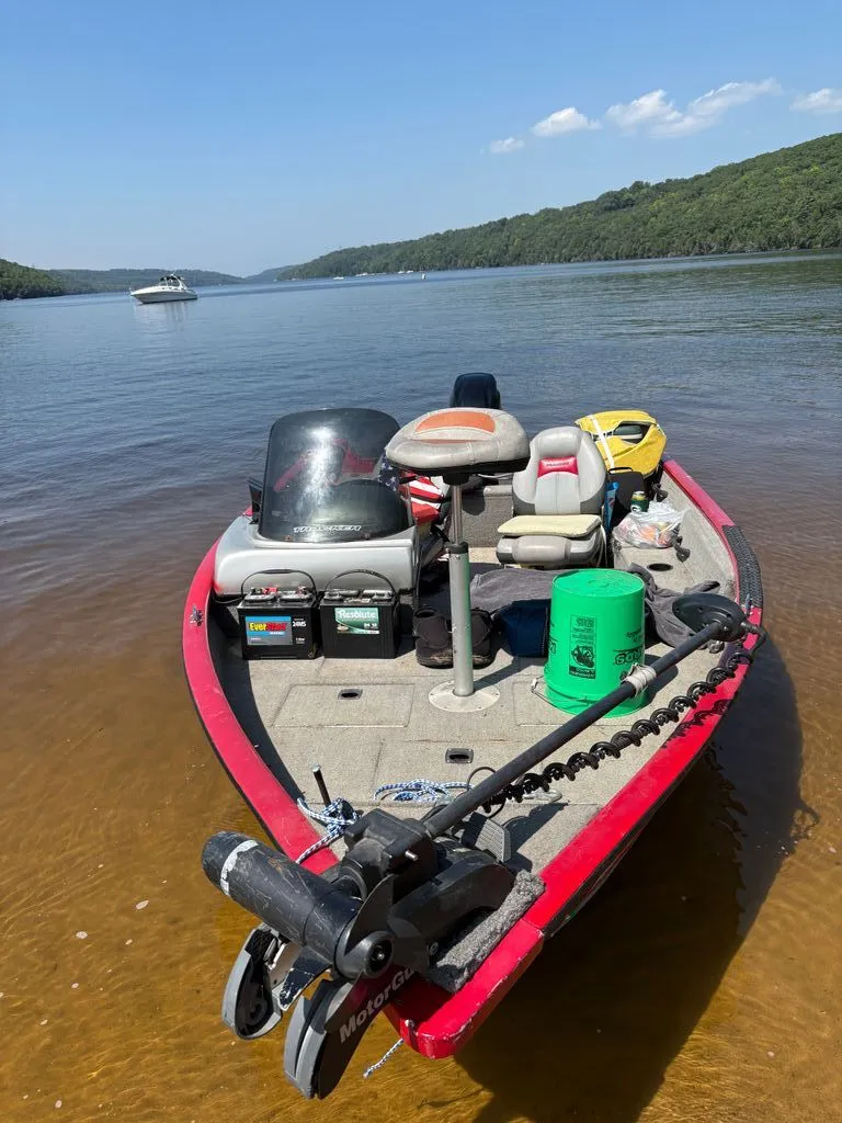 Slide: The Image of A red fishing boat is docked at a calm lake shore with wooded hills in the background. - 8