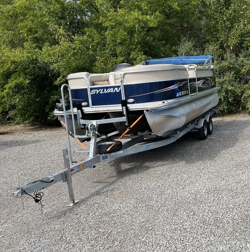 Slide: The Image of A 2011 Sylvan 8520 Cruise pontoon boat on a trailer, surrounded by trees. - 2