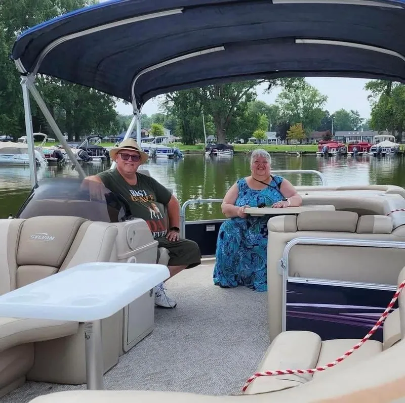 Slide: The Image of Two people sit on a pontoon boat with beige interior and blue sunshade. - 9