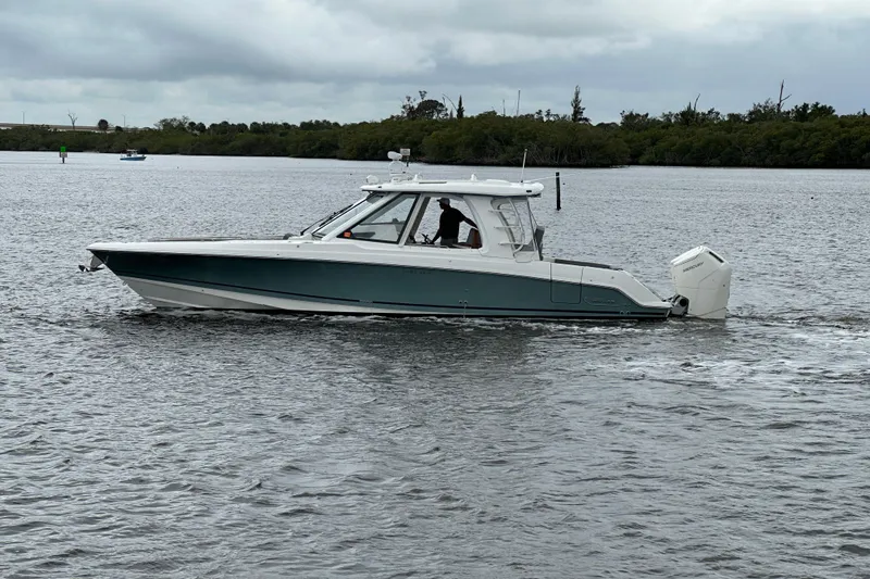 The Image of 2024 Boston Whaler 380 Realm cruising on a calm river under cloudy skies. - 0