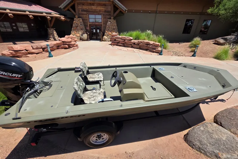 Slide: The Image of 2024 Tracker Grizzly 1754 SC boat with Mercury engine, parked outside a rustic building. - 11