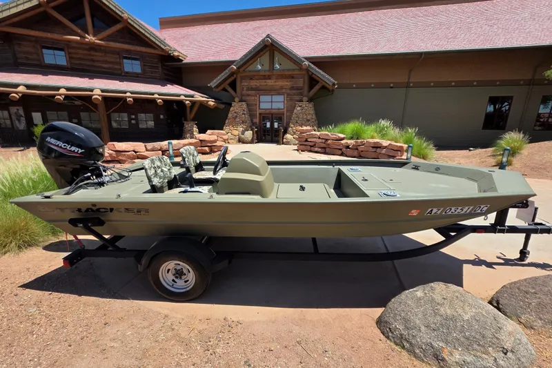 Slide: The Image of 2024 Tracker Grizzly 1754 SC boat with Mercury engine, parked outside a rustic building. - 8