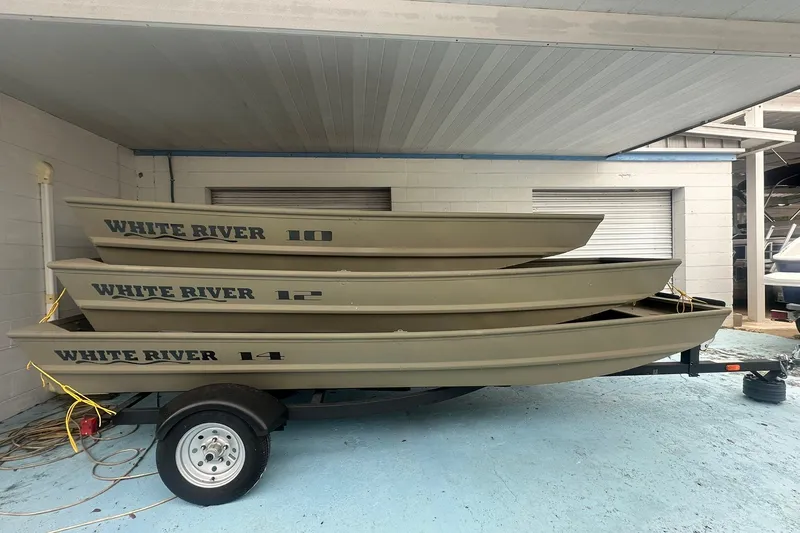 Slide: The Image of Stacked White River TOPPER 1542 Jon Boats, 2025 models, on a trailer in a garage. - 7