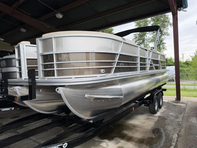 The Image of A silver pontoon boat is on a trailer in a covered area. - 1