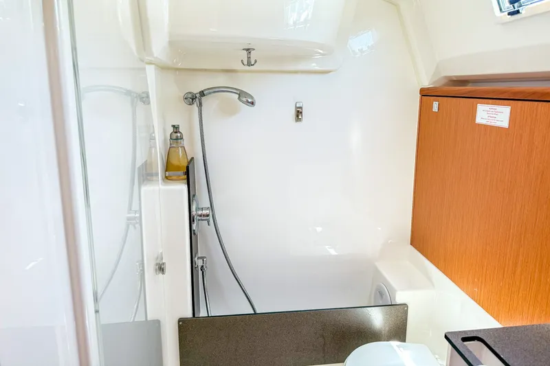 Slide: The Image of The image shows a bathroom on a 2014 Bavaria Cruiser 37 with a shower and wooden cabinet. - 27