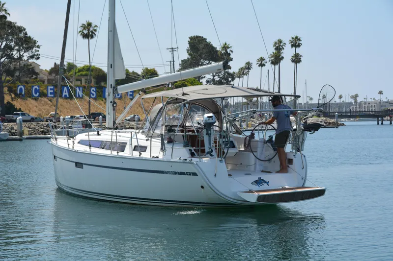Slide: The Image of A 2014 Bavaria Cruiser 37 sailboat navigating a harbor with palm trees in the background. - 2