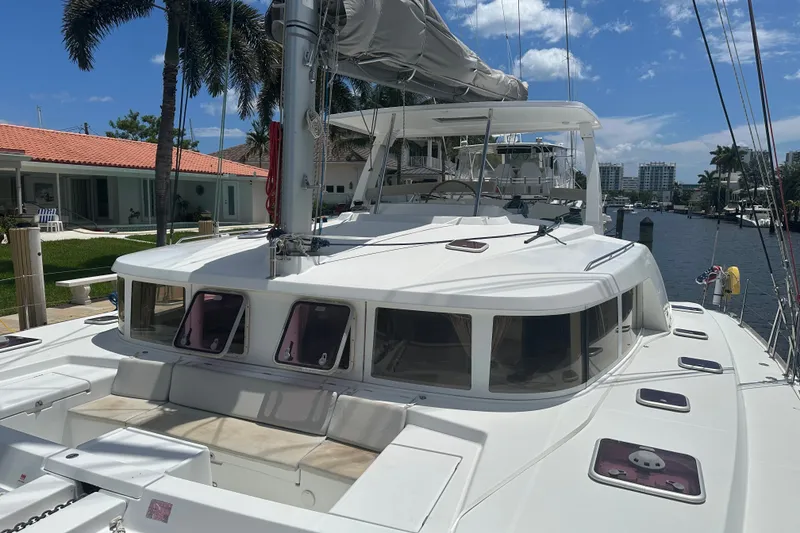 Slide: The Image of 2010 Lagoon 440 catamaran docked by waterfront homes under a clear blue sky. - 77