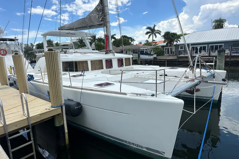 Slide: The Image of 2010 Lagoon 440 catamaran docked at marina, clear sky, palm trees in background. - 75