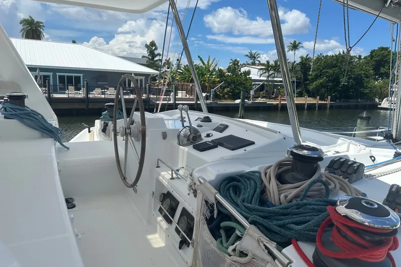 Slide: The Image of Cockpit of 2010 Lagoon 440 catamaran with steering wheel and ropes, docked by waterfront homes. - 80