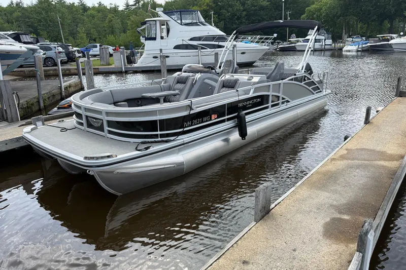 Slide: The Image of 2023 Bennington 25RTSB pontoon boat docked at a marina, surrounded by other boats. - 2