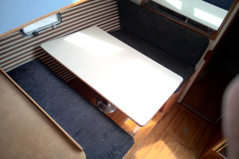 Slide: The Image of 1986 CHB Ponderosa boat interior with dining area, featuring a table and cushioned seating. - 30