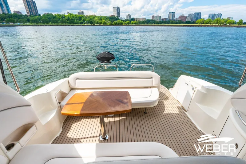 Slide: The Image of The image shows the aft deck of a 2005 Sea Ray 360 Sundancer with a wooden table and seating. Water and a cityscape are visible in the background. - 17