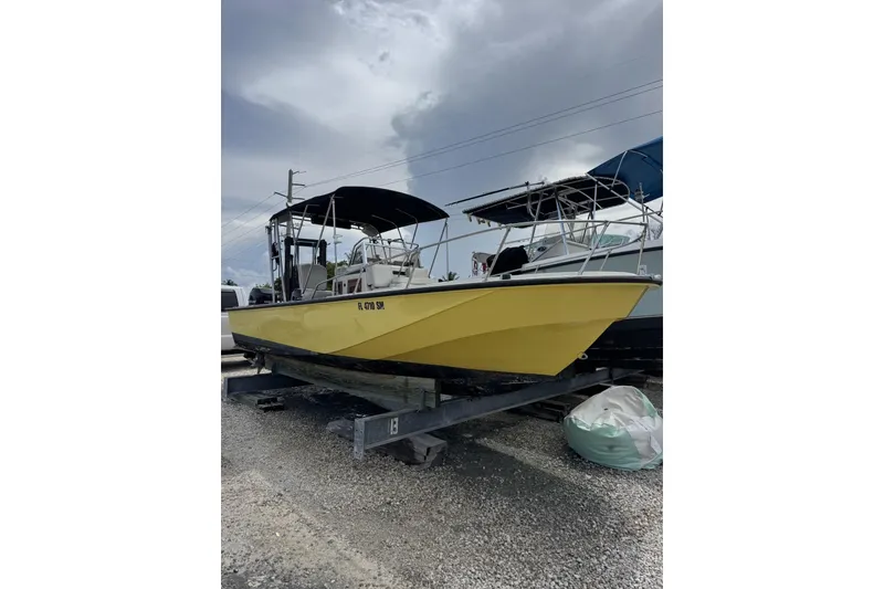 Slide: The Image of 1983 Boston Whaler 21 Outrage boat in yellow, parked on a gravel lot under cloudy skies. - 7