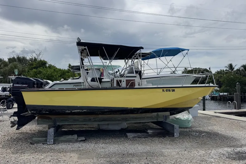 The Image of 1983 Boston Whaler 21 Outrage boat with yellow hull on a dock, under cloudy skies. - 1
