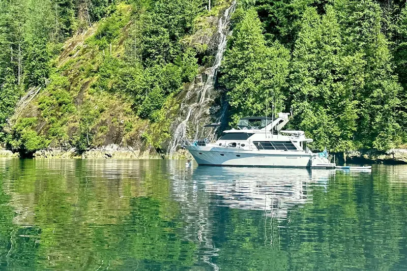 Slide: The Image of Luxury Symbol 50 Pilothouse yacht anchored by lush forested cliffs, reflecting on calm water. - 31