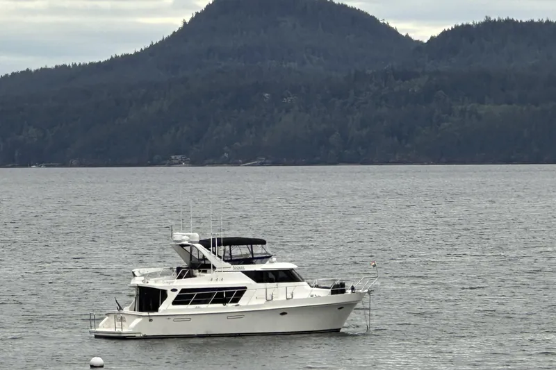 Slide: The Image of A 2000 Symbol 50 Pilothouse yacht anchored on a calm lake with forested hills. - 32