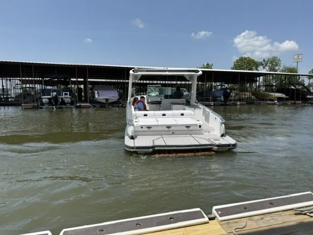 Slide: The Image of A 2021 Aviara AV32 on calm water. Covered boat slips are visible in the background. - 13