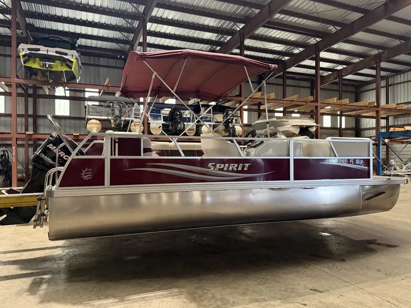 Slide: The Image of A 2011 JC Spirit pontoon boat with a red canopy in a warehouse. - 13