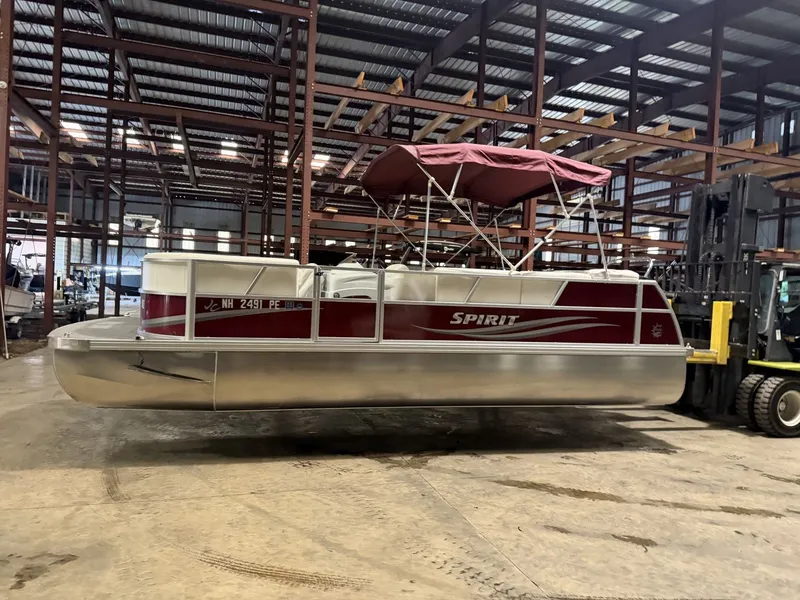 Slide: The Image of A 2011 JC Spirit pontoon boat with a red canopy is in a warehouse. - 9