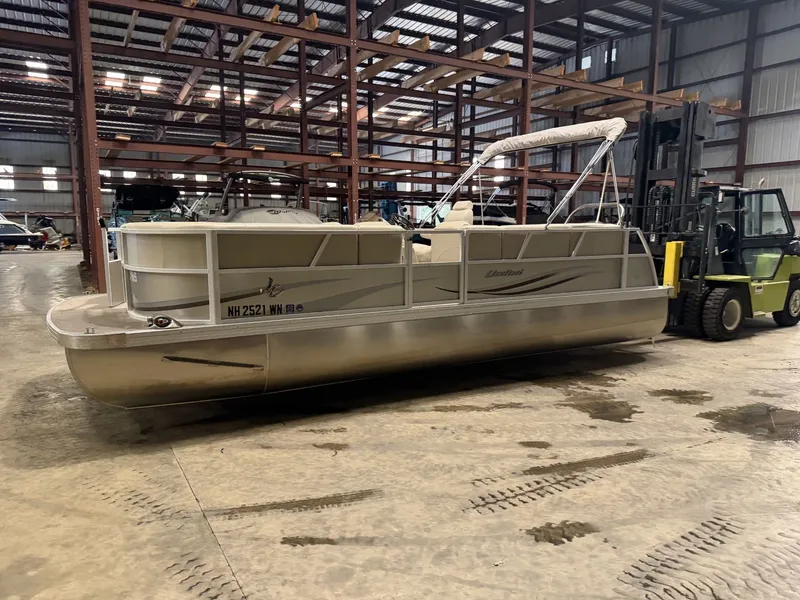 The Image of A pontoon boat is parked in a warehouse next to a forklift. - 1