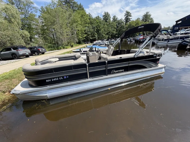 The Image of A 2014 Premier 240 SunSation pontoon boat is docked by a calm lakeside. - 1