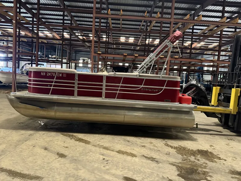 Slide: The Image of A red Starcraft pontoon boat in a warehouse, placed on a forklift. - 18