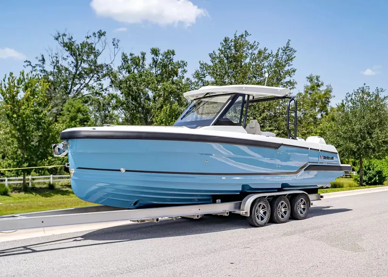 The Image of A 2027 Wellcraft 28 T-Top boat on a trailer, surrounded by trees and a clear sky. - 1
