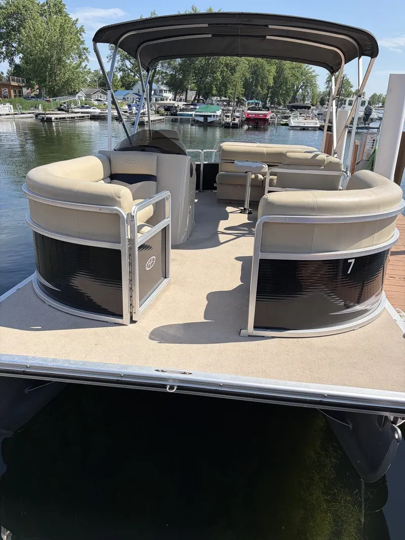 Slide: The Image of A 2012 Harris FloteBote Cruiser 200 CX200 docked. It features beige seating and a black railing. - 2