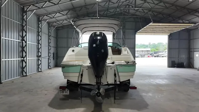Slide: The Image of A 2023 NauticStar 243 DC boat in a warehouse, featuring an outboard motor and a Bimini top. - 8