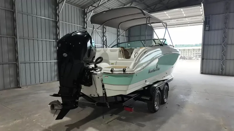 Slide: The Image of A 2023 NauticStar 243 DC boat in a warehouse. It features an outboard motor and a bimini top. - 3