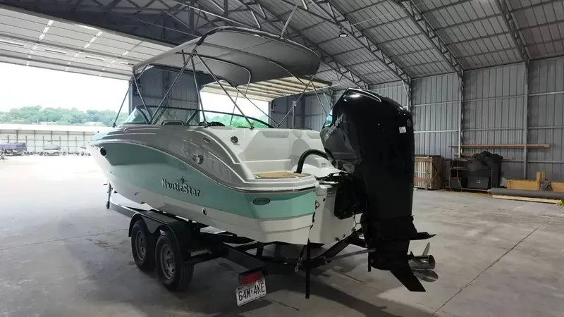 Slide: The Image of A 2023 NauticStar 243 DC boat in a storage facility, featuring an outboard motor and bimini top. - 9