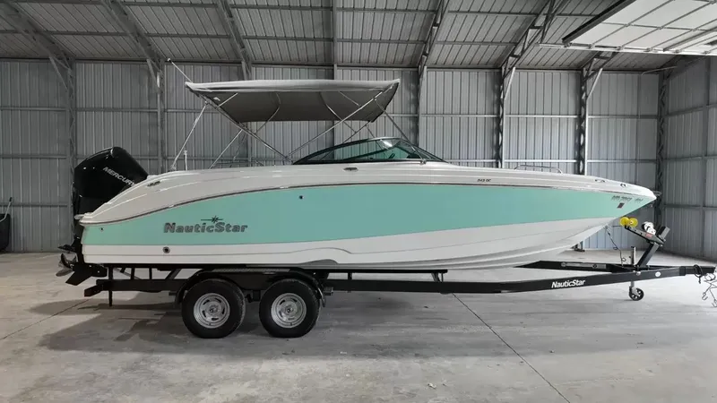 The Image of A 2023 NauticStar 243 DC boat in a warehouse. It features a turquoise and white paint job. - 1