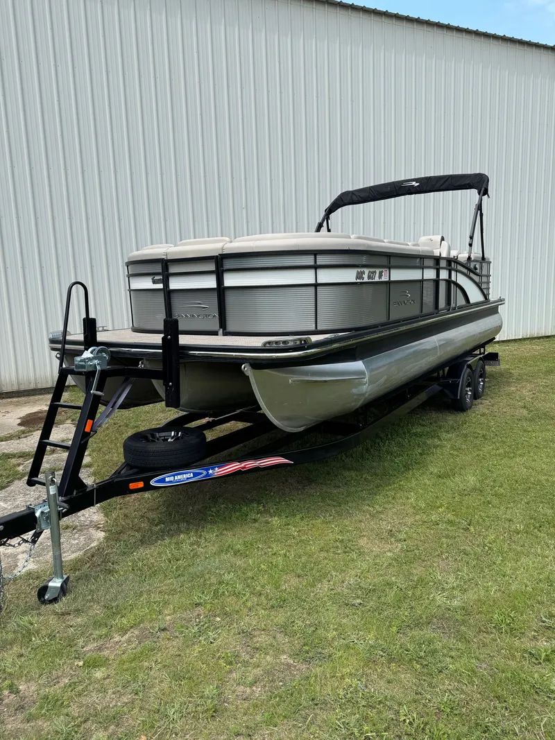 The Image of A 2019 Bennington 25RSR pontoon boat on a trailer, parked on grass near a building. - 1
