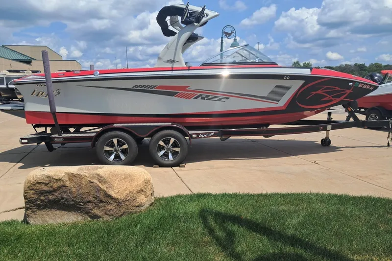 Slide: The Image of 2013 Tigé RZ2 boat on trailer, parked outdoors under a partly cloudy sky. - 2