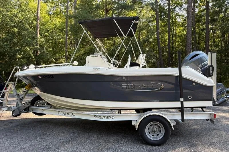 The Image of 2022 Robalo R180 Center Console boat on trailer in wooded area. - 1