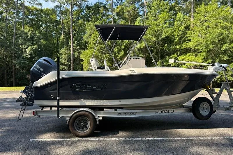 Slide: The Image of 2022 Robalo R180 Center Console boat on trailer, parked in wooded area. - 5