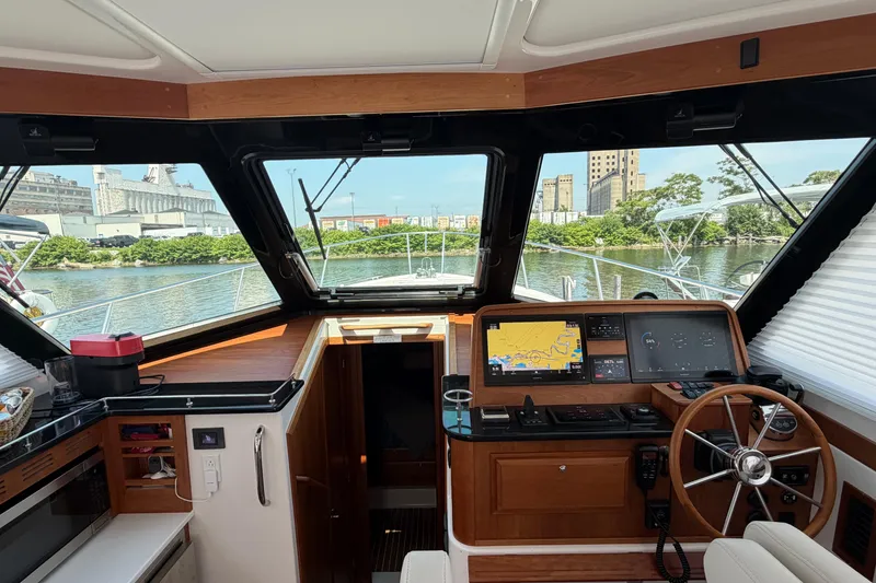 Slide: The Image of 2024 Back Cove 372 helm with navigation screens, steering wheel, and waterfront view. - 59