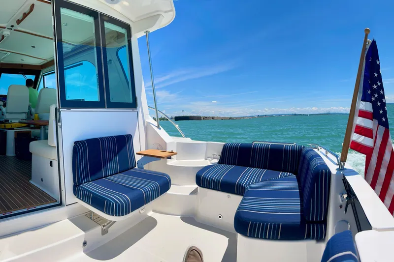 Slide: The Image of 2024 Back Cove 372 yacht with striped seating, American flag, and ocean view. - 8